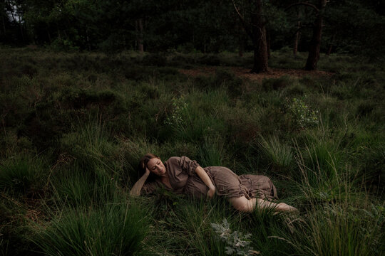 Pregant woman resting in tall grass wearing a brown dress