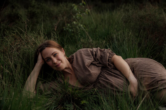 Pregant woman resting in tall grass wearing a brown dress