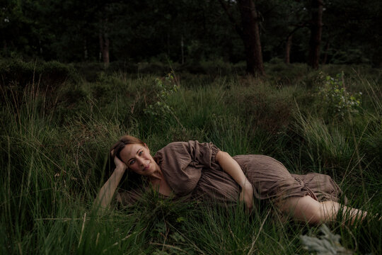 Pregant woman resting in tall grass wearing a brown dress