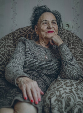 An elderly woman sits thoughtfully inside