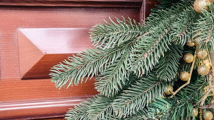 Close-up of green spruce branches with golden decorative berries on a brown wooden door background