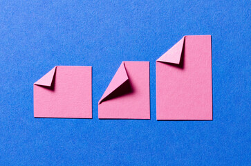 Pink paper message notes or sheets with folded edge dog-ear earmark and copy space for text on blue background, top view flat lay conceptual desk backdrop