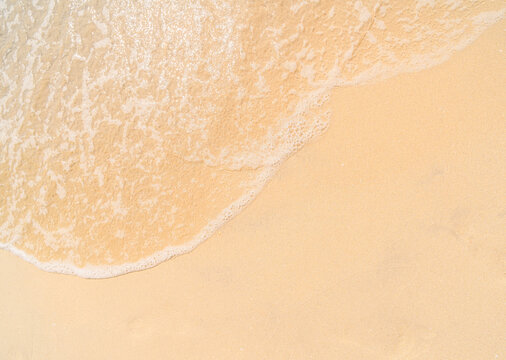 A close-up, high-angle of a gentle white-foamed ocean wave washing onto a smooth sandy beach