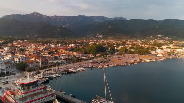 Golden sunrise aerial pan over Limenas port and town center on Thasos Island, Greece, capturing the picturesque Aegean Sea coastline and anchored boats.