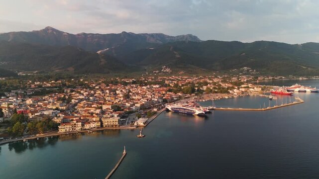 Tranquil aerial pan out from Limenas town and port, Thasos Island, Greece, revealing the coastal landscape and Aegean Sea during a vibrant summer sunrise.