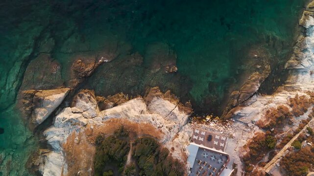 Aerial top-down drone view of the rugged coastline and turquoise Aegean Sea near Limenas, Thasos Island, Greece, illuminated by summer sunrise.