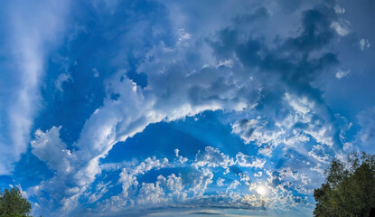 White high-altitude clouds almost completely obscure blue sky. Light vapor appears against blue background. Arch cumulus cloud curves cloudscape panoramic across wide field view atmospheric spectacle.