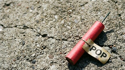A single red firecracker with the word POP written on its label rests on a cracked concrete surface.