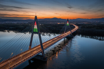 Budapest, Hungary - Aerial view of Megyeri Bridge illuminated in festive Hungarian national colors in honor of the 1848 March 15th Revolution and War of Independence at sunset with blue and golden sky