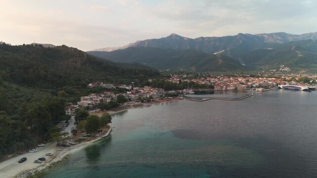 Aerial drone approach shot over the Aegean Sea towards Limenas, the picturesque port and capital town of Thasos Island, Greece, at golden summer sunrise.