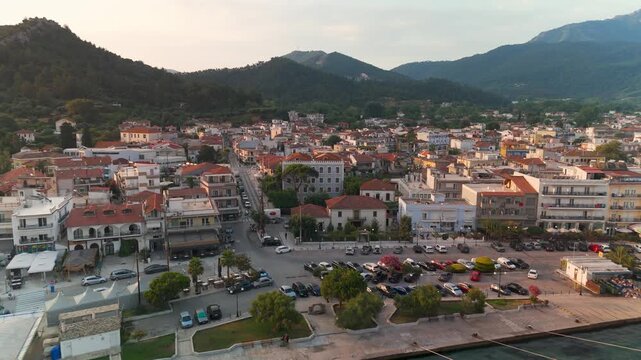Aerial drone flyover of the picturesque Limenas harbor and coastal town on Thasos Island, Greece, illuminated by the golden light of a summer sunrise.
