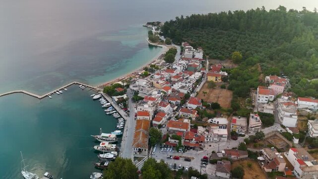Scenic aerial drone approach and descent toward the historic Old Port of Limenas, Thasos Island, Greece, bathed in golden light at summer sunrise.