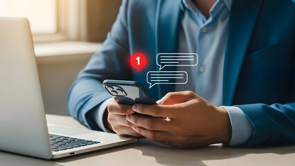 Businessman checking notifications on phone with laptop nearby