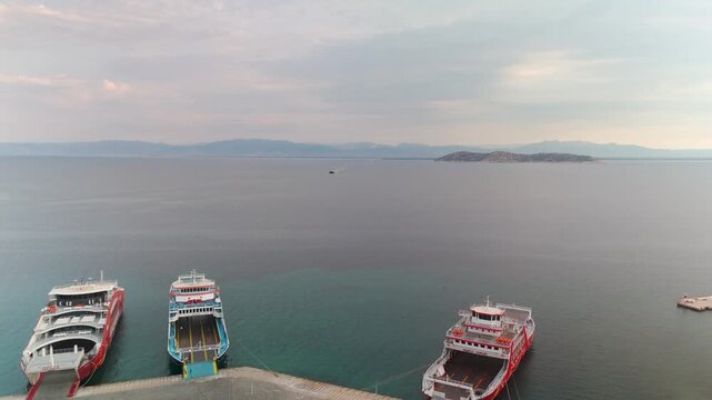 Aerial drone flight panning away from Limenas harbor and Thasos Island, heading over the Aegean Sea towards the mainland of East Macedonia, Greece, during a serene summer sunrise.