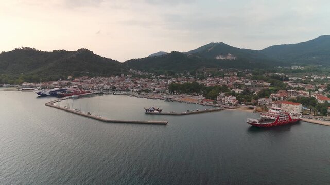 Picturesque aerial view of Limenas harbor and coastal town on Thasos Island, Greece, bathed in warm golden light during a serene summer sunrise over the Aegean Sea.