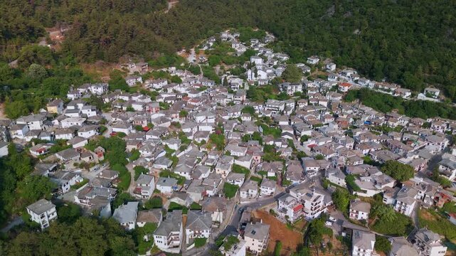 High altitude aerial drone panorama panning across the traditional Greek village of Panagia, nestled on the forested slopes of Mount Ipsarion, Thasos Island, Greece.