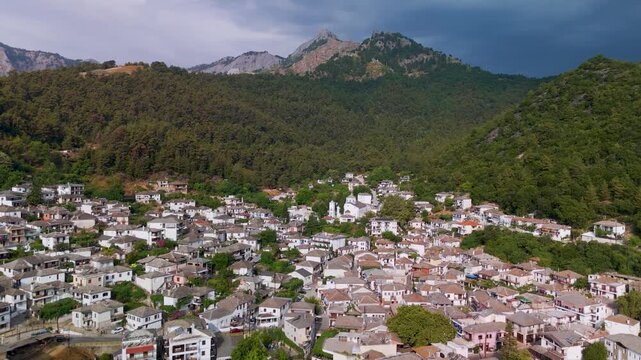 Aerial drone descent shot flying down toward the traditional stone houses and church of Panagia village, nestled on the densely forested slopes of Mount Ipsarion, Thasos Island, Greece.