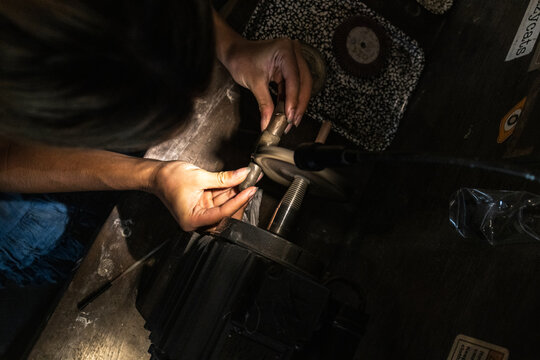 Overhead view of artisan hands shaping a metal ring on a bench tool in a Bali, Indonesia jewelry workshop. Industrial handmade craftsmanship scene showing traditional metalworking 