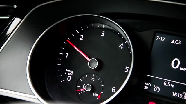 Car dashboard interior detail. Tachometer gauge with red needle shows engine revolutions. Digital screen displays time, temperature, and vehicle mileage data
