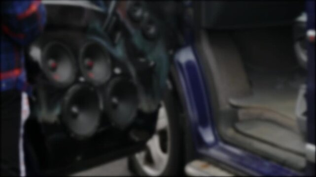 Custom car audio system speakers on open car door. Multiple black speakers installed, aftermarket modification for enhanced sound, deep bass. Professional setup for powerful music, blurry