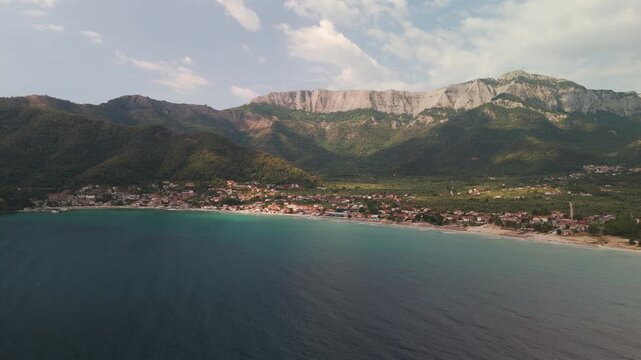 Scenic aerial drone view panning across the turquoise waters of Golden Beach Bay towards the densely forested slopes of Mount Ipsarion on Thasos Island, Greece.