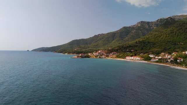 Scenic aerial drone approach toward coastal homes nestled near Kinira village on the lush, forested coastline of Thasos Island, Greece, overlooking the Aegean Sea.