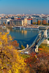 Obraz premium Budapest cityscape, panoramic view of city and Danube River with Chain bridge and beautiful architecture in autumn season, trees, branches and yellow leaves in foreground