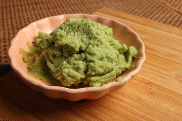 Traditional wasabi sushi sauce in a small dish, featuring a vibrant green color and smooth texture on wooden bad bamboo mat