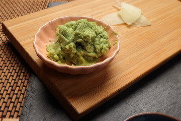 Traditional wasabi sushi sauce in a small dish, featuring a vibrant green color and smooth texture on wooden bad bamboo mat