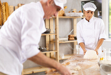 Man and woman, experienced bakers, prepare dough for baguettes and croissants together in private bakery