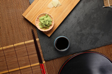 wasabi sushi soya sauce in a small dishes plate, featuring a vibrant green color  texture on dark slate wooden board bed bamboo mat copy text space