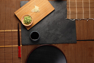 wasabi sushi soya sauce in a small dishes plate, featuring a vibrant green color  texture on dark slate wooden board bed bamboo mat copy text space