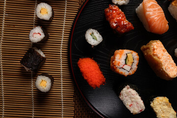 High-quality close-up of fresh assortment sushi rolls served on a dark plate, featuring vibrant colors, fresh fish, laid on slate board bamboo mat chopsticks