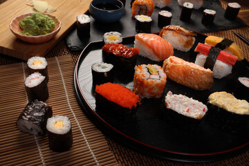 High-quality close-up of fresh assortment sushi rolls served on a dark plate, featuring vibrant colors, fresh fish, laid on slate board bamboo mat chopsticks