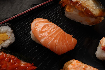 High-quality close-up of fresh assortment sushi rolls served on a dark plate, featuring vibrant colors, fresh fish, laid on slate board bamboo mat chopsticks