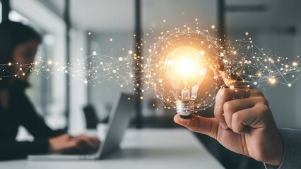 Hand holding a glowing light bulb with network connections, symbolizing innovation and business ideas in a modern office setting.