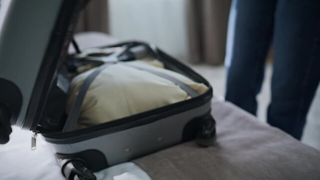 Woman hands unpacking suitcase on motel bed closeup. Smiling lady taking clothes