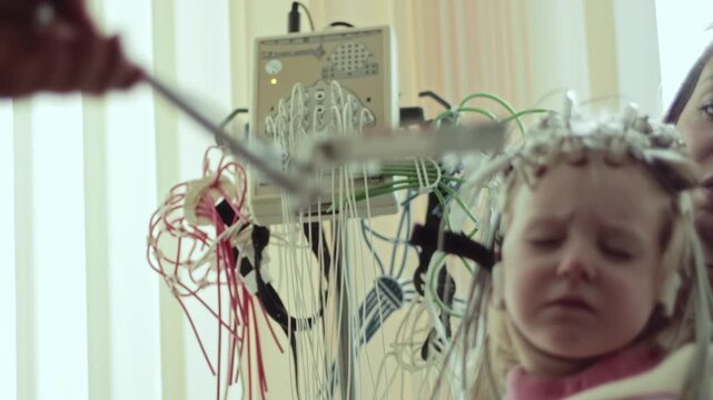 Medical professional conducts electroencephalography on young child. Electrodes on head of patient record brain electrical activity. Diagnostic procedure for neurological conditions.