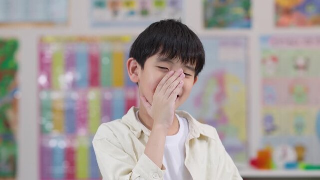 Shy Schoolboy Covering Face in Colorful Classroom Setting