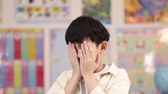 Stressed Schoolboy Covering Face with Hands in Classroom