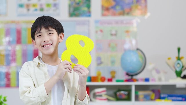 Smiling Schoolboy Holding Foam Number Eight in Classroom