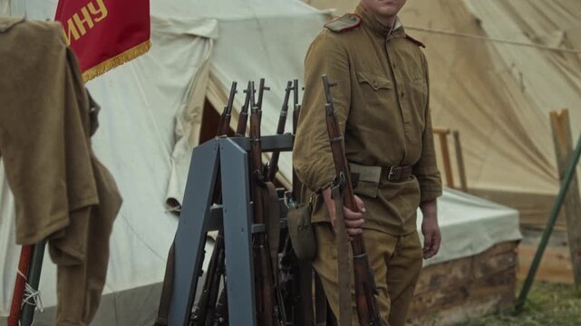 Depiction of a Red Army private soldier in Soviet military uniform and pilotka hat, holding a Mosin rifle, performing guard duty during a Great Patriotic War reenactment
