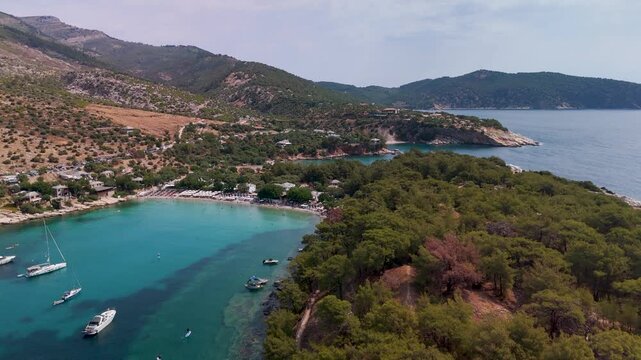 Aerial drone pan out revealing the picturesque coves and beaches of Alyki Peninsula, Thasos, Greece, surrounded by lush forest and the turquoise Aegean Sea.