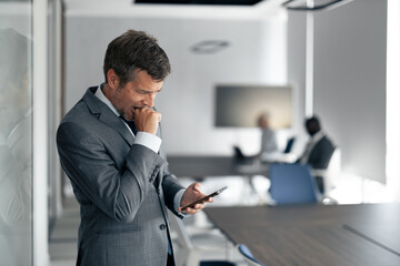 Fototapeta premium Coughing Businessman Checks Phone in Modern Office During Busy Workday