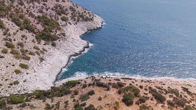 Aerial drone shot over the rugged coastline near Giola Lagoon and Astris village on Thasos Island, Greece, featuring the clear blue Aegean Sea.