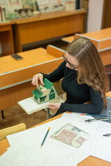Caucasian young woman making a model of a building. Student of the construction university. 