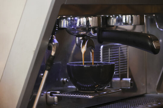 Professional espresso machine brewing fresh hot coffee into dark cup showing classic morning routine and barista process with aromatic liquid stream pouring from metal portafilter inside cafe shop - Powered by Adobe