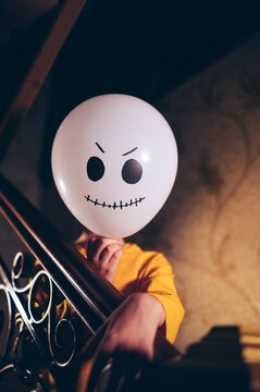 Child holding ghost face balloon in Halloween costume on stairway indoors