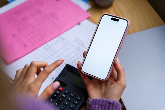 Person using calculator and smartphone for budgeting and financial planning
