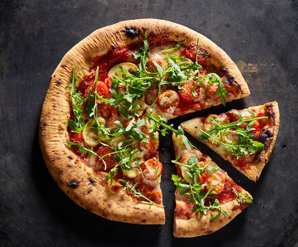 Neapolitan pizza with arugula, tomato and mushroom on rustic surface